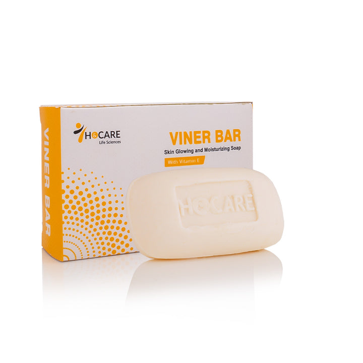 A bar of HOCARE Viner Bar skin glowing and moisturizing soap in an off-white color, shown in front of its orange and white retail packaging box on a reflective white surface.