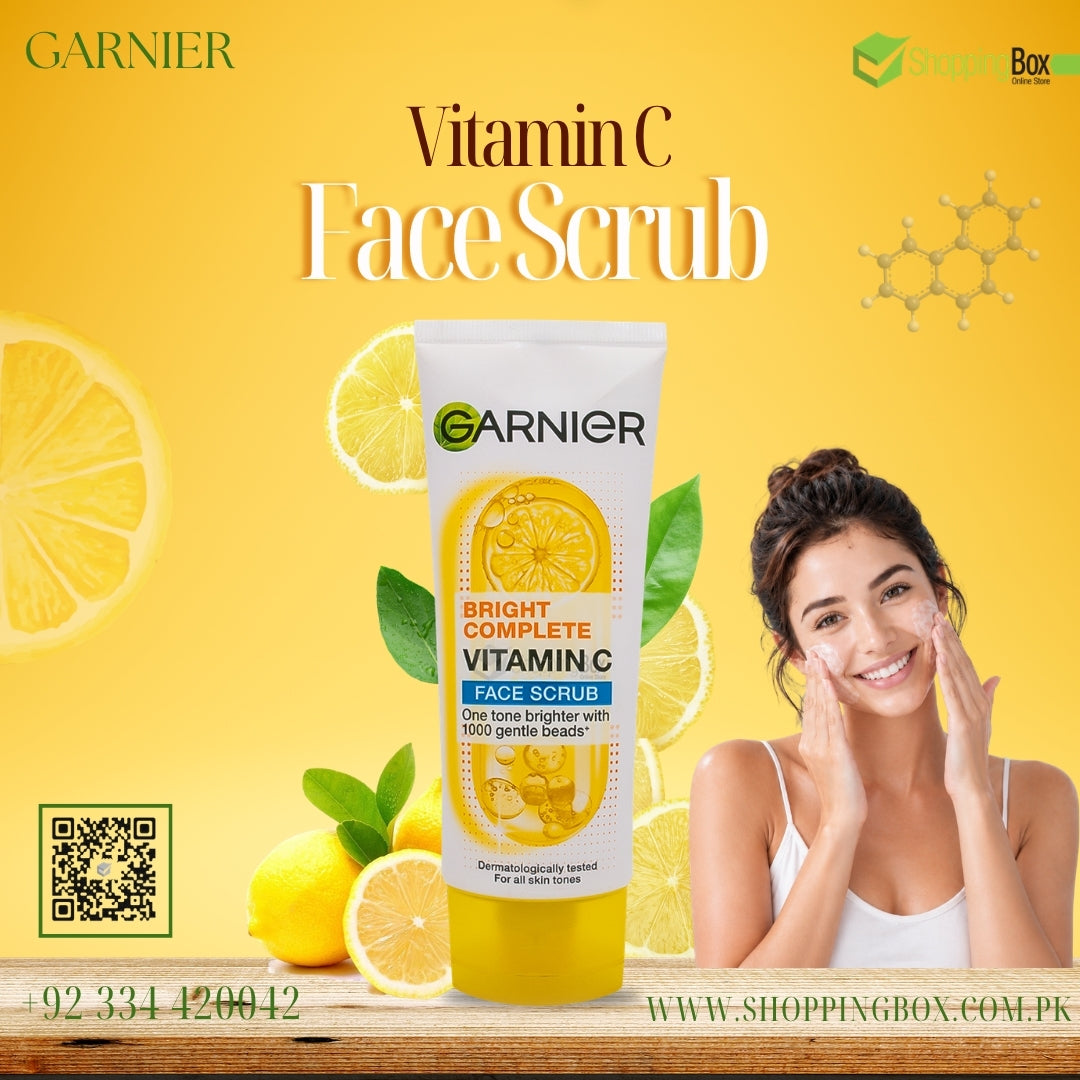 Garnier Vitamin C Face Scrub in a white squeeze tube with yellow liquid, set against a bright yellow background with lemon slices, a smiling woman applying cream to her face, and promotional text.